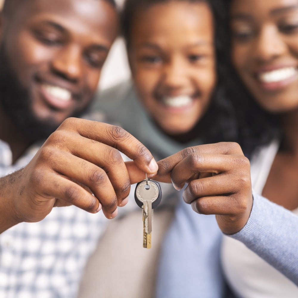 Happy african american family holding keys from their new home Housing concept. Happy black family with daughter holding keys from their new home, selective focus on hands, closeup.