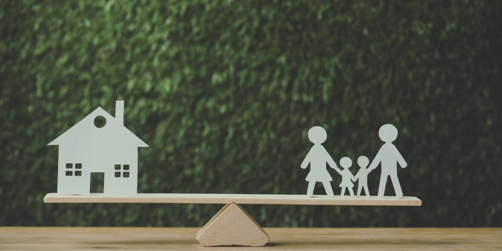 paper cut house and paper family balancing on seesaw on green background paper cut house and paper family balancing on seesaw on green background