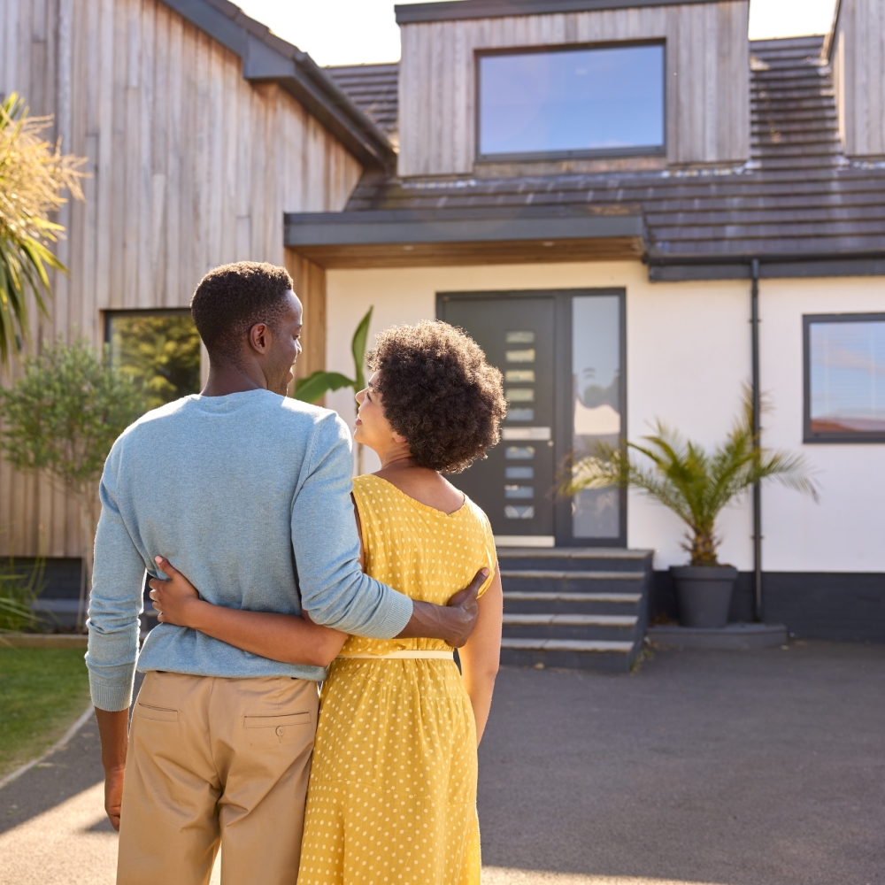 Rear View Of Couple Standing In Driveway In Front Of Dream Home Together Rear View Of Couple Standing In Driveway In Front Of Dream Home Together